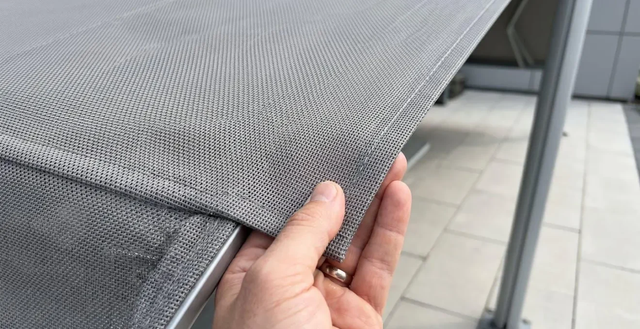 Detalle en primer plano de la textura de un tejido técnico de toldo con trama microperforada visible bajo luz natural